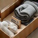 Beautifully arranged gift box filled with ethical textile goods like a small blanket, a candle, and a wellness tea, ready for gifting.