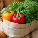Stacked reusable jute shopping bags with fresh organic vegetables, representing eco-friendly choices
